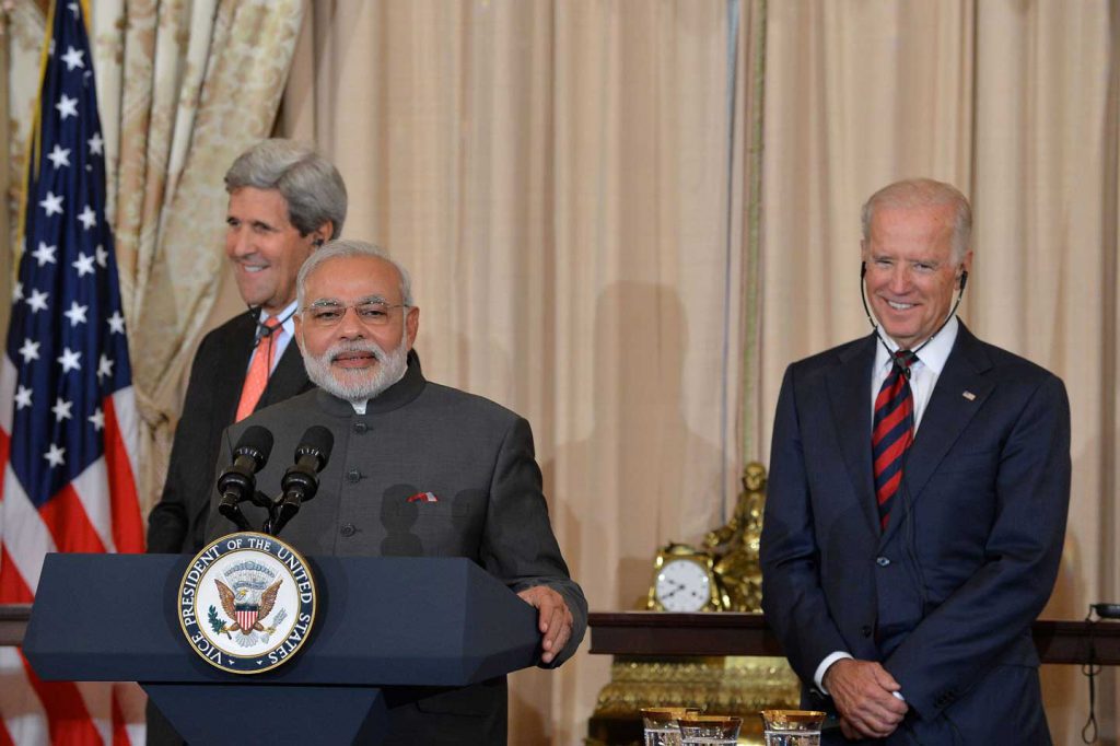 John Kerry, Narendra Modi, and Joe Biden standing at a podium