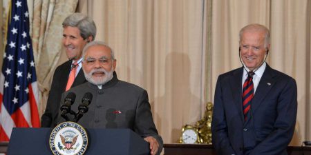 John Kerry, Narendra Modi, and Joe Biden standing at a podium