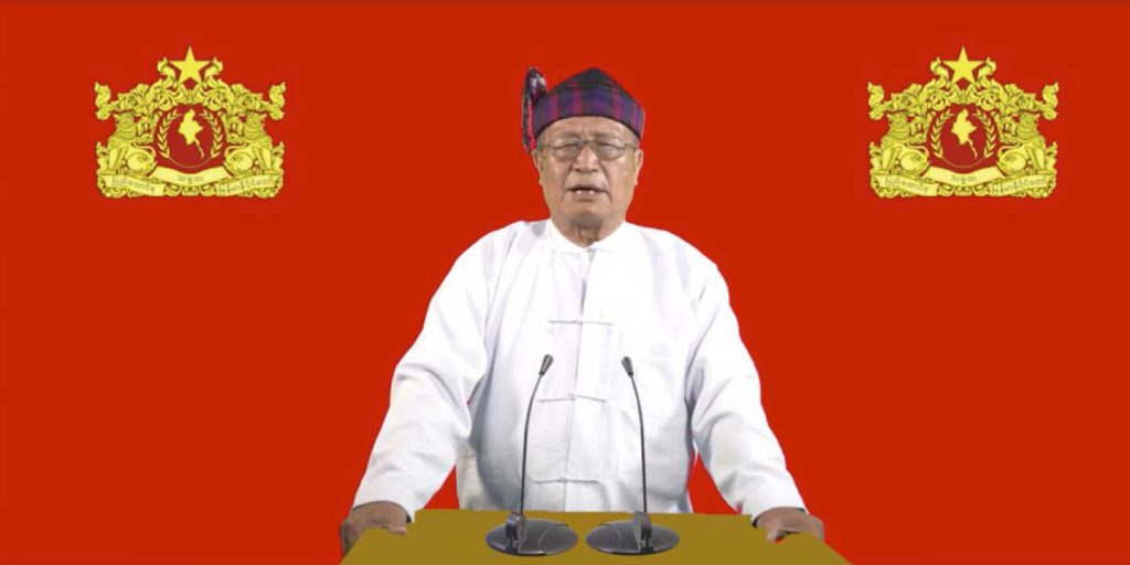 Duwa Lashi La standing at podium with red background