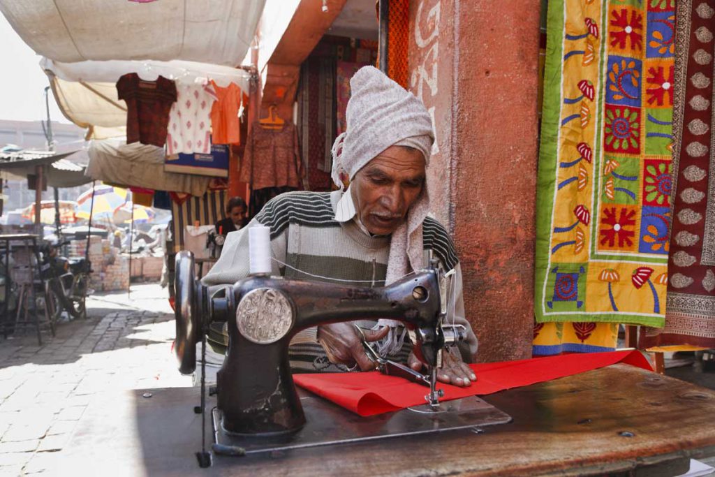 An elderly man using a sewing machine at an outdoor shop