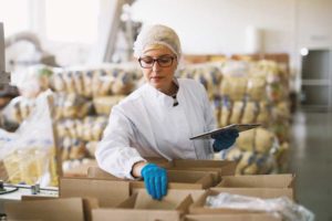 An inspector in hairnet and lab coat reviewing box contents
