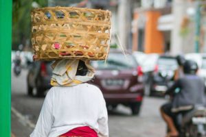A person walking down street carrying a basket on their head