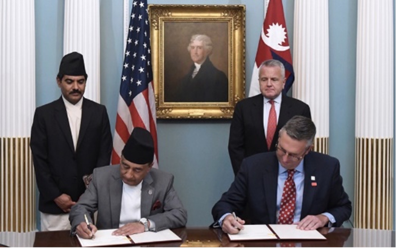 Nepalese and American statesmen signing documents in front of a portrait of George Washington